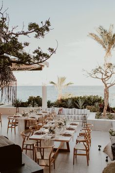 an outdoor dining area with tables and chairs overlooking the ocean in front of palm trees