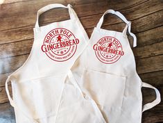 two white aprons sitting on top of a wooden table next to each other with gingerbread printed on them