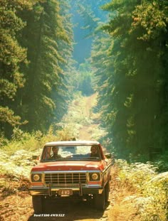 a red truck driving down a dirt road next to tall pine tree lined forest on both sides