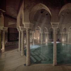 an indoor swimming pool surrounded by pillars and arches with lights on the ceiling above it