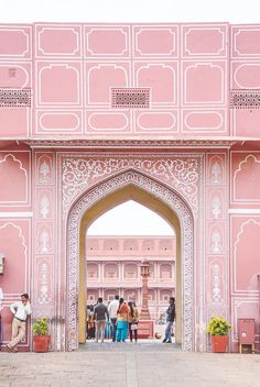 people are standing in front of a pink building with white trim and intricately carved archways