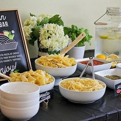 a table topped with bowls filled with pasta and veggies next to a chalkboard sign