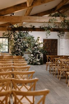 rows of wooden chairs are lined up in the middle of a room with flowers and greenery