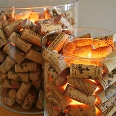 two glass vases filled with wine corks and lit candles on a wooden table