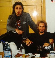 two men sitting next to each other at a table with food and drinks on it