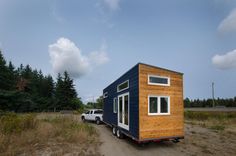 a tiny house is parked in the middle of a field next to a truck and trees