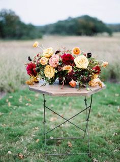 a wooden table topped with flowers on top of a lush green field covered in grass