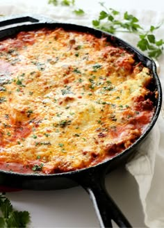 a skillet filled with cheese and sauce on top of a white cloth next to parsley