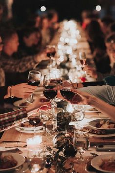 a group of people sitting at a long table with wine glasses in their hands and plates on the table