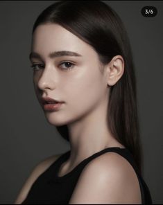 a woman with long brown hair wearing a black top and posing for a photo in front of a gray background