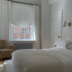 a white bed sitting next to a window in a room with two chairs and a radiator