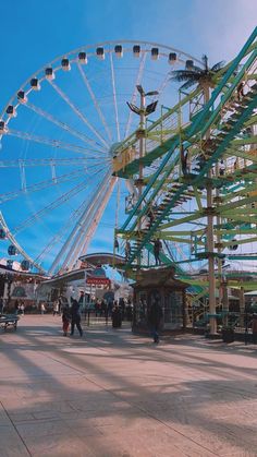 a ferris wheel sitting in the middle of a park with people walking around and looking at it