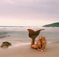 a beautiful woman laying on top of a sandy beach next to the ocean with an eagle statue