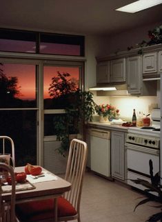 a kitchen with an oven, table and chairs in it at night time as the sun sets