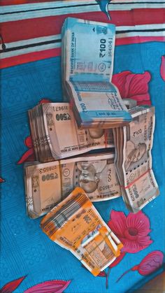 a pile of money sitting on top of a blue and red table cloth with flowers