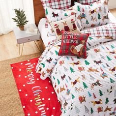 a bed with christmas themed comforters and pillows on top of it, next to a red rug