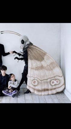 three people standing next to each other in front of a giant moth costume on the wall