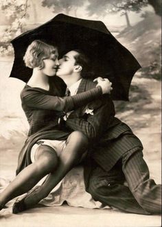 an old black and white photo of a man kissing a woman with an umbrella over her head