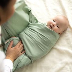 a woman holding a baby wrapped in a green wrap on top of a white blanket