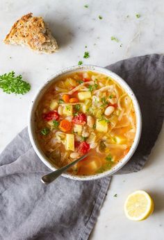 a white bowl filled with soup next to a piece of bread and lemon wedges