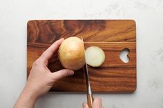 a person cutting onions with a knife on a wooden cutting board next to a white wall