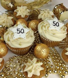 cupcakes with white frosting and gold decorations are on a table next to golden sequins