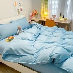 a bed with blue sheets and pillows in a room next to a table with stuffed animals on it