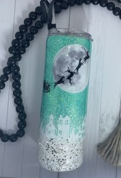 a green and white tumbler sitting on top of a wooden table next to a black beaded necklace