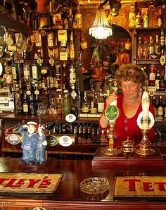 a woman holding two beer mugs in front of a bar filled with liquor bottles