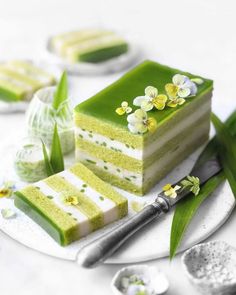 a piece of green cake on a white plate with flowers and spoons next to it