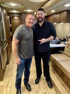 two men standing next to each other in a room with wood flooring and cabinets