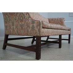 an upholstered chair with wooden legs and arm rests on the floor in front of a wall