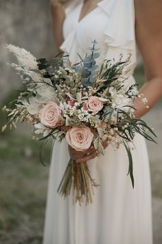 a woman in a white dress holding a bouquet of flowers and greenery on her wedding day