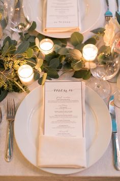 the table is set with silverware, candles and menu cards for dinner guests to enjoy