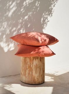 two orange pillows sitting on top of a wooden stump in front of a white wall