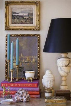 a table topped with books next to a lamp and pictures on the wall behind it