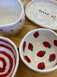 three bowls with strawberries painted on them sitting on a wooden table next to each other