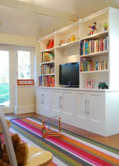 a living room with bookshelves, television and toy cars on the floor in front of it