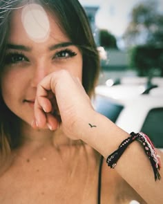 a woman with a small black bird tattoo on her left wrist and right hand near her face