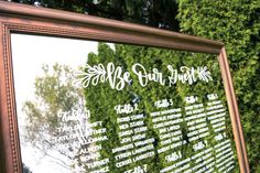 a large mirror reflecting the names and dates of people in front of some green trees