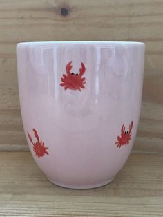 a pink bowl with red crabs painted on the side and inside, sitting on a wooden surface