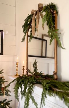 a fireplace mantel decorated for christmas with greenery, candles and mirror in the background