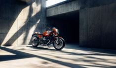 an orange and black motorcycle parked in front of a concrete building with sunlight coming through the windows