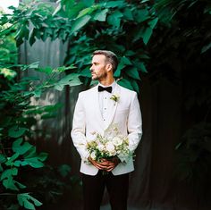 a man in a white tuxedo holding flowers