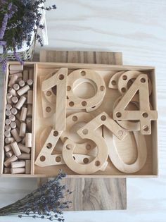 the wooden letters and numbers are in a box next to lavender flowers on a table