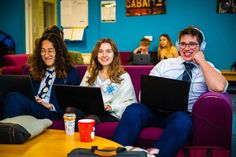 three people sitting on a couch with laptops