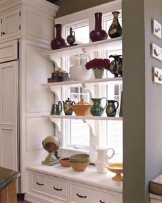 a kitchen filled with lots of white cupboards and dishes on top of shelves next to a window