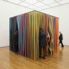 two people standing next to each other in front of an art piece that looks like multicolored sticks