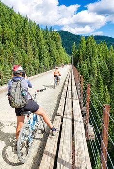 two people riding bikes on a bridge over a river