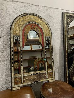 an ornate mirror and stool in front of a white wall